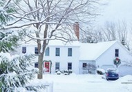 White house surrounded by evergreen trees and covered in snow.