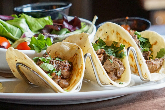 Plate of three tacos on a white plate with a bowl of salad next to it.
