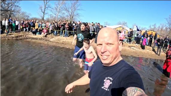 Firefighter in the Fox River with a crowd of people on shore.
