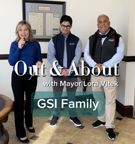 Mayor holding a microphone and interviewing two men from a local company with text on screen.