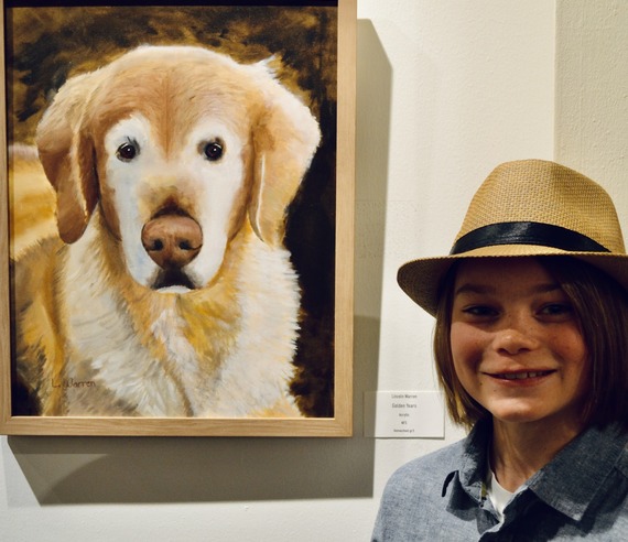 A boy poses with his painting of a golden retriever.