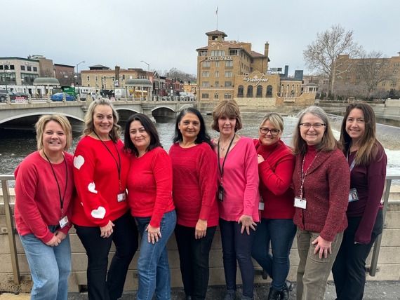 A group of women stand in front of the Fox River wearing red.