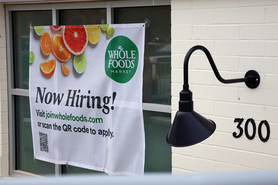 Whole Foods "now hiring" sign draped across window of building.