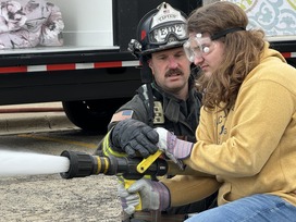 A firefighter and student use a firehose during a training program.