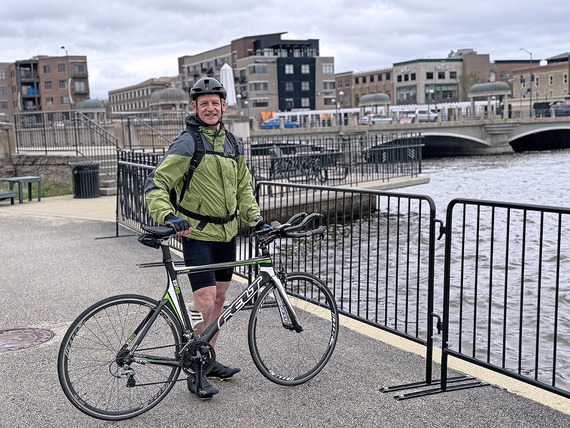 A man stands with his bike with the Fox River behind him.