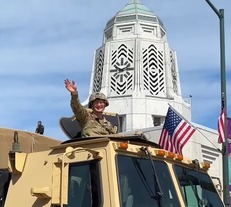 A US soldier waves from a large truck in front of the Municipal Building during the parade.