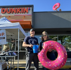 A person holding an inflatable donut stands on a rooftop with two people from the Police Department in the foreground.