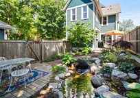 A green Victorian House with a pond and cobbled patio.