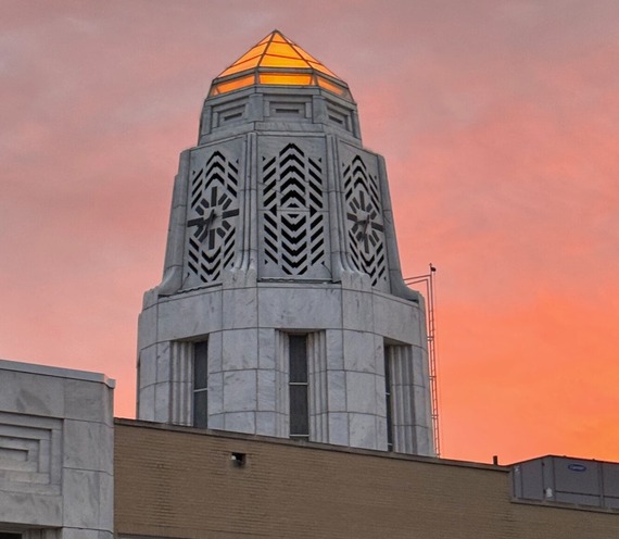 Municipal building tower is lit up in orange to match the orange sky of the setting sun.