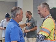 The mayor talks to a public works employee who is smiling with two other men in the background.