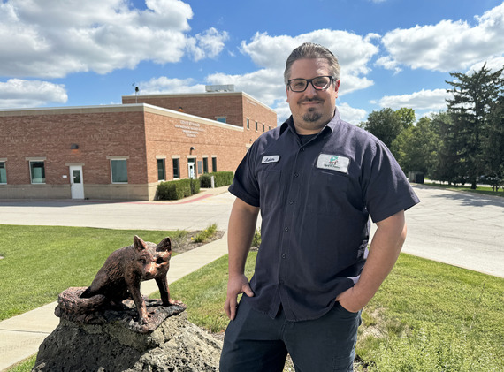 A man stands on a hill overlooking a public works building and a sculpture of a fox.