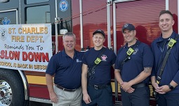 The Mayor and three firefighters stand in front of a firetruck with a sign that is reminding motorists to slow down.