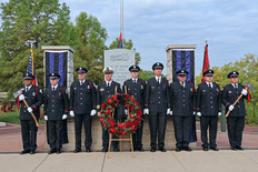 Firefighters stand next to memorial wreath during 9/11 ceremony.