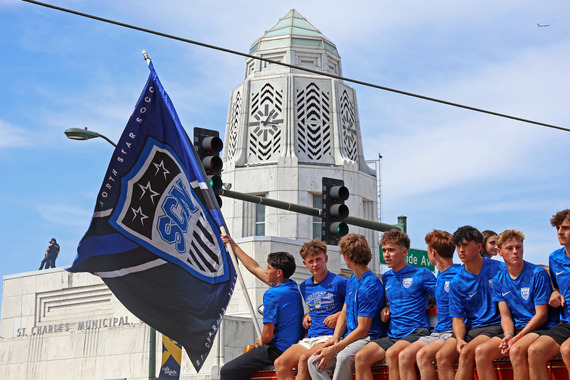Soccer players hold a flag as they pass by city hall.