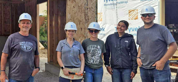 Volunteers in hard hats pose for a photo in front of a construction site.