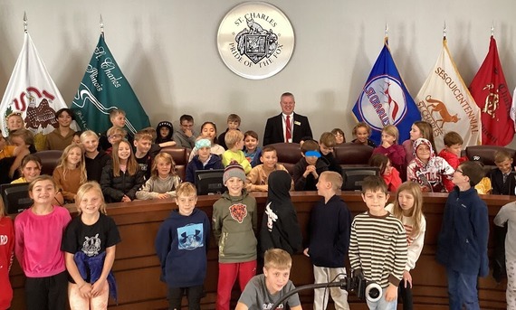 A group of kids poses with the Mayor in Council Chambers.