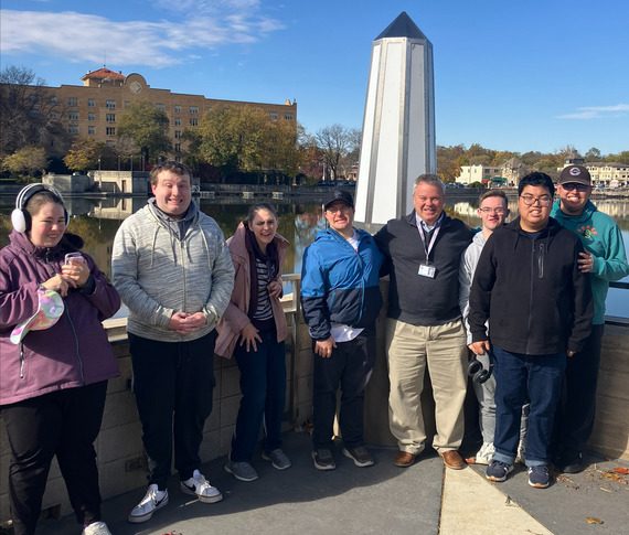 The Mayor stands shoulder to shoulder with other adults in front of the Fox River.