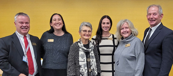 The mayor and other city leaders and volunteers pose for a photo in front of a yellow wall.