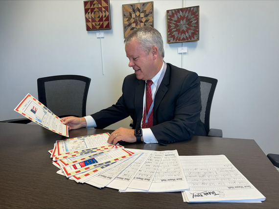 The Mayor sitting behind a desk reads a stack of thank you cards from students.