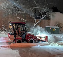 A parking lot gets cleared of snow at night at the old police station site.