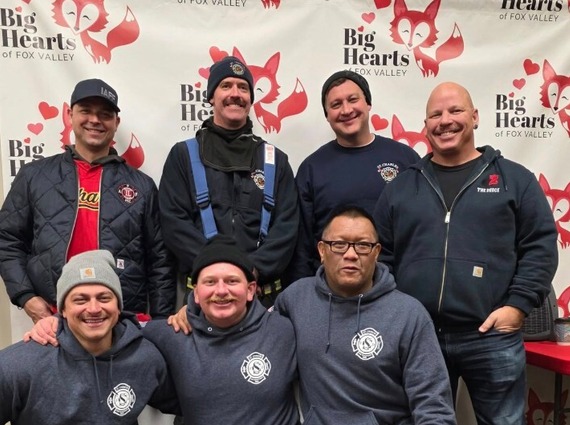 Firefighters pose in front of a Big Hearts of Fox Valley step and repeat wall during an event.