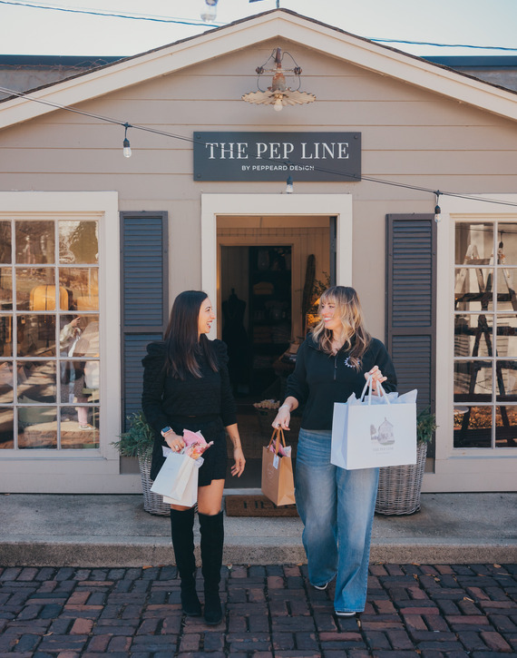 Two women stand outside of a retail boutique with shopping bags.