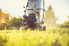 The bottom half of a person mowing a lawn with the lawn mower in the foreground.