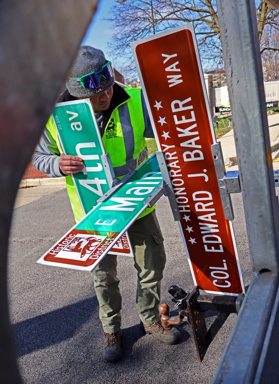 A Public Services employee installs a new honorary street sign featuring Col. Baker.