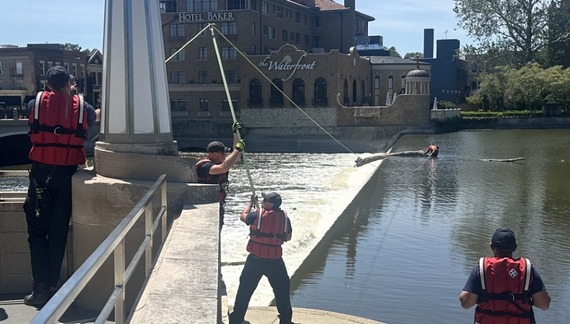 Firefighters remove an oversized log from being lodged at the edge of the dam in the Fox River.