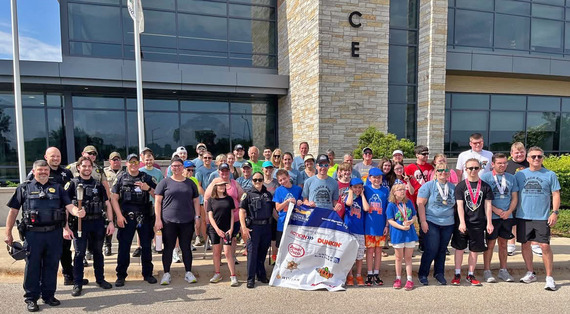 A group of people participating in the special olympics torch run stand in front of the police department.