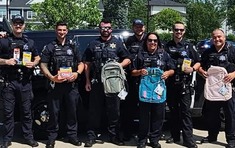 A group of officers poses with the backpacks that were stuffed into the squad cars for charity.