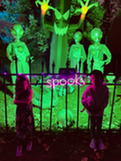 A neon green yard decorated with aliens and a spooky sign in pink with two little girls in front of it.