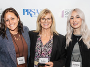 Three women hold an award in front of a step-and-repeat sign.
