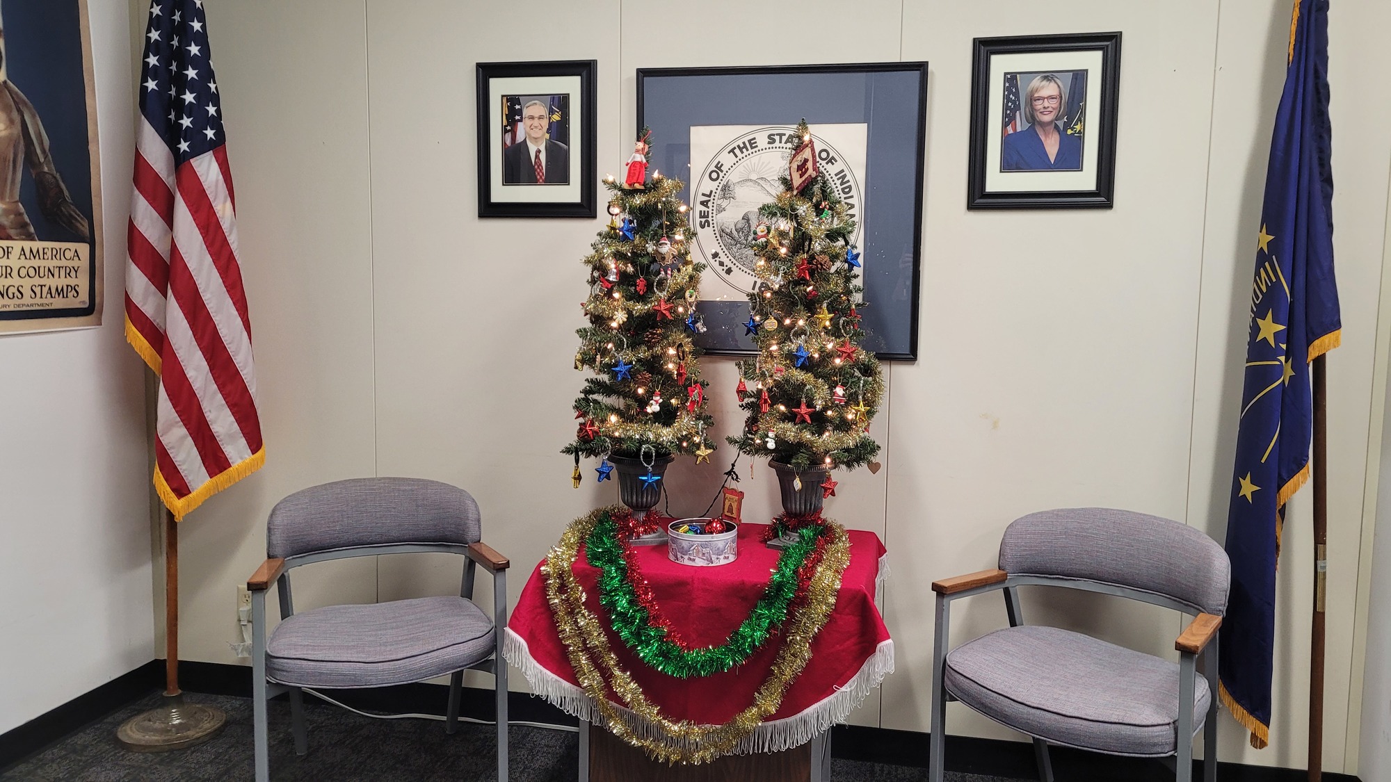 IARA office Christmas trees in front of the Indiana State Seal, with guest chairs on either side, and behind them, the U.S. flag and a photo of Gov. Eric Holcomb on the left, and a photo of Lt. Governor Suzanne Crouch and the Indiana State flag on the right.