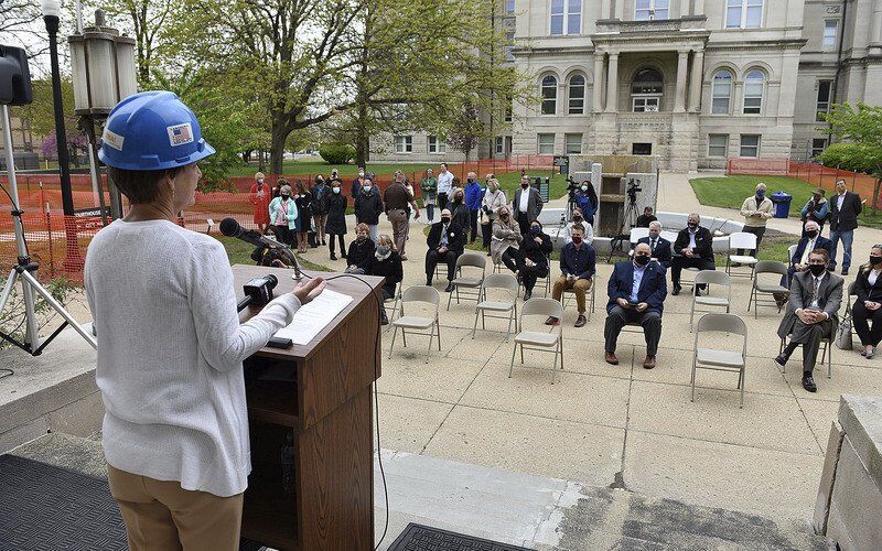 Mary Kramer stands at a podium and addresses a socially-distanced crowd. 