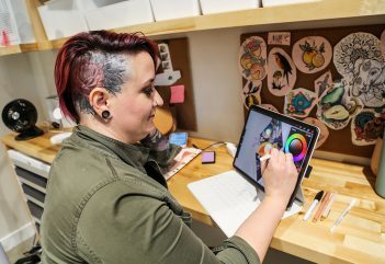 Woman with short dyed hair and tattoos creates design on an ipad