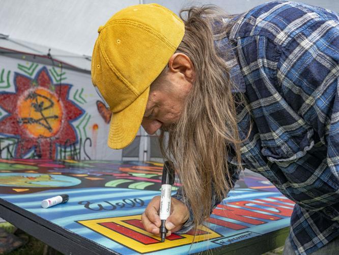 man in yellow baseball cap and blue flannel drawing on mural with sharpie