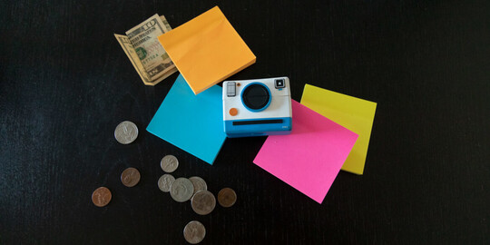 Flat lay image of camera, sticky notes, and money 