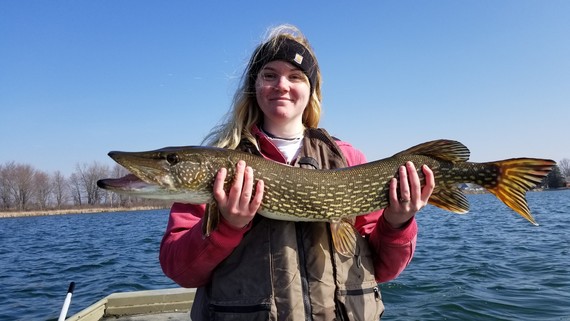 Woman holding a large pike boating on a wintery lake