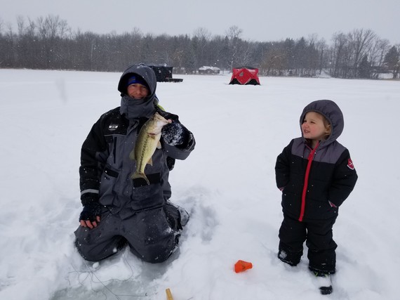 Angler holding a bass on an iced-over lake with his young daughter