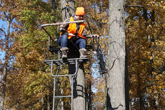 A woman dressed in hunter orange sitting on a tree stand.
