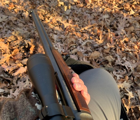 A hand holding a muzzleloader with leaves in the background.