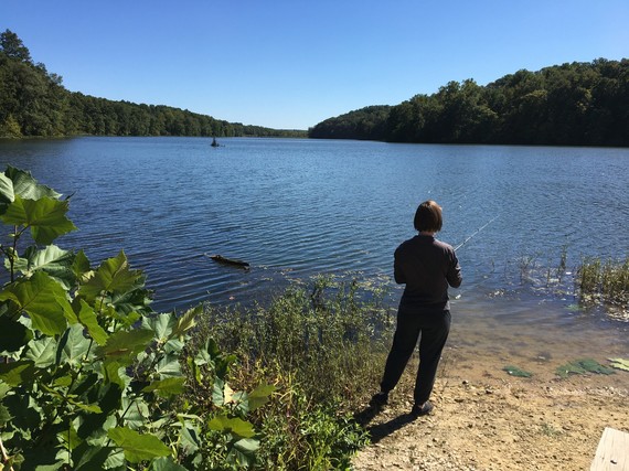 A woman shoreline fishing on a sunny day.