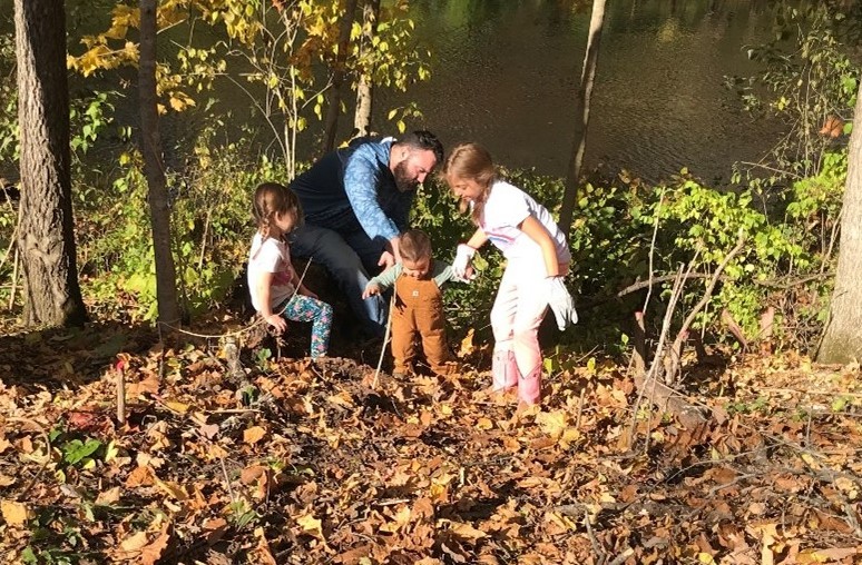 A man and three children wearing gloves and volunteering in the woods.