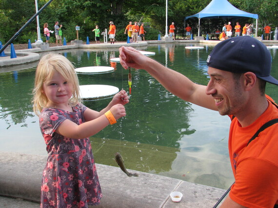 A young girl and a smiling man holding a fishing line together.