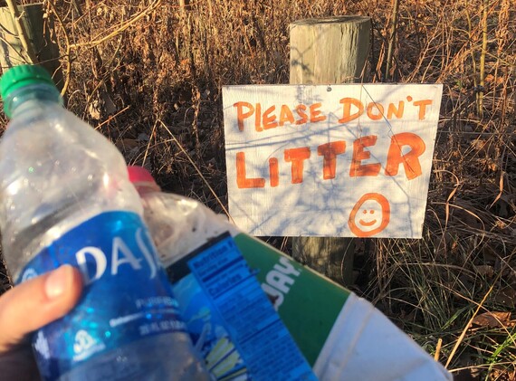 A â€œPlease donâ€™t litterâ€ sign behind a hand holding plastic bottles.