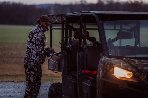 A hunter standing beside a camouflaged vehicle.