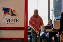 Image of a woman walking into a polling location, with a Vote sign