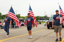 Image of three men, holding American flags, walking in the parade
