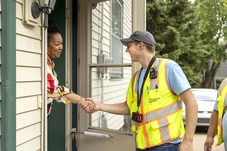 Community Action employee in a neon vest meets an elderly resident